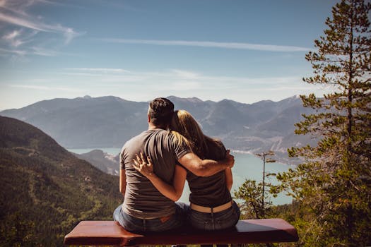 Attachment styles in relationships; Couple sitting on bench embracing scenic mountain view, embodying romantic nature escape.