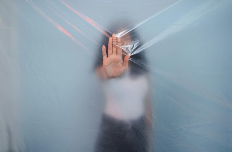 Blurred image of a woman pressing her hand against a translucent plastic sheet, creating a surreal effect.
